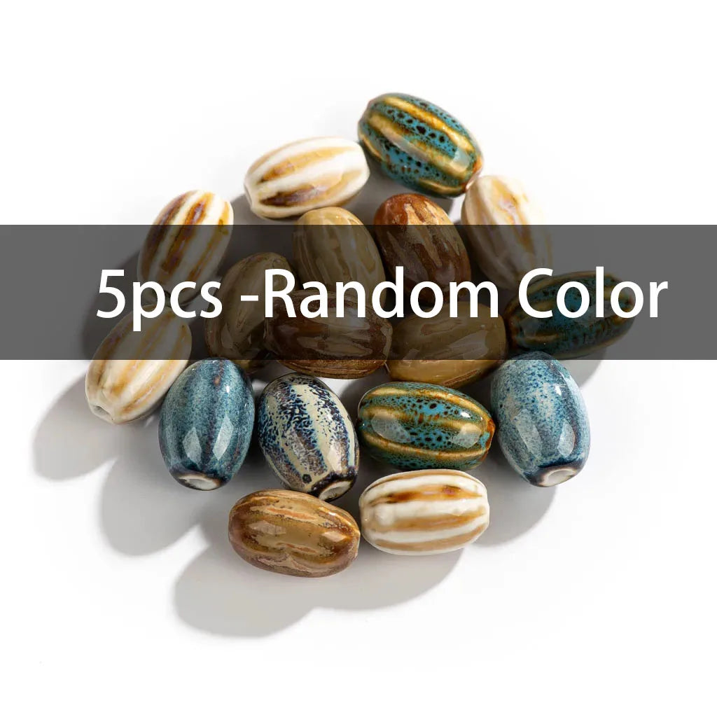 A pile of five decorative glass beads in various colors and patterns, including blue, brown, beige, and green, with a dark gray text banner overlay reading '5pcs -Random Color' across the middle.