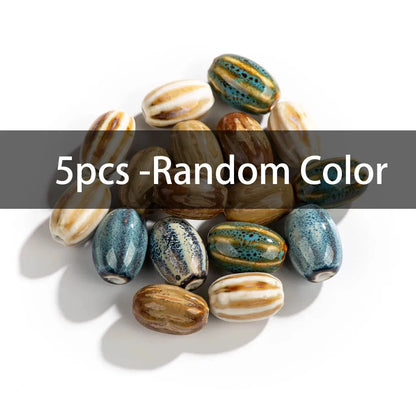 A pile of five decorative glass beads in various colors and patterns, including blue, brown, beige, and green, with a dark gray text banner overlay reading '5pcs -Random Color' across the middle.