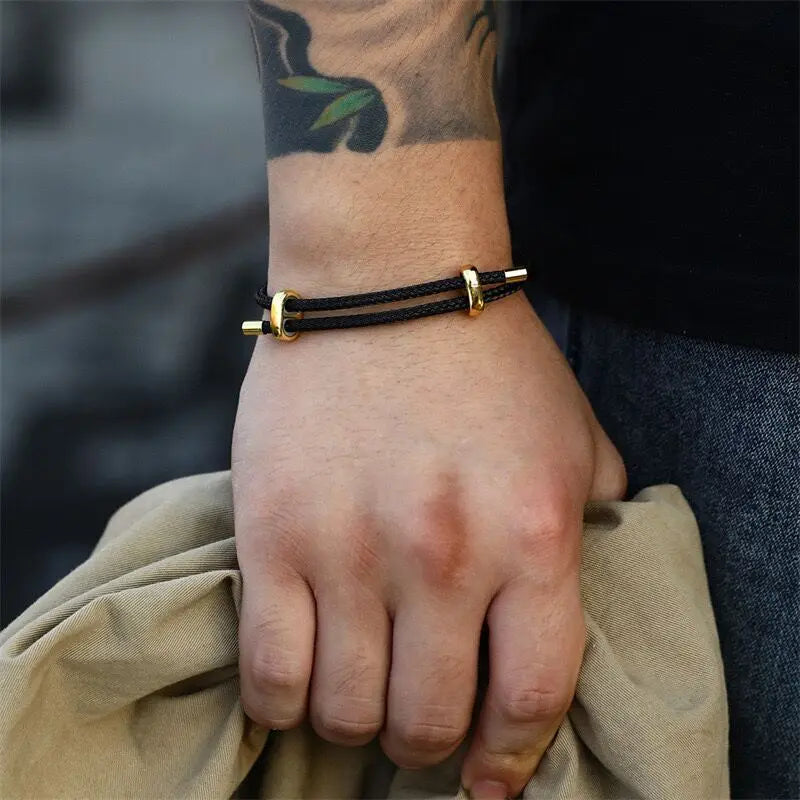 Hand wearing a black cord bracelet with gold clasps, blurred background