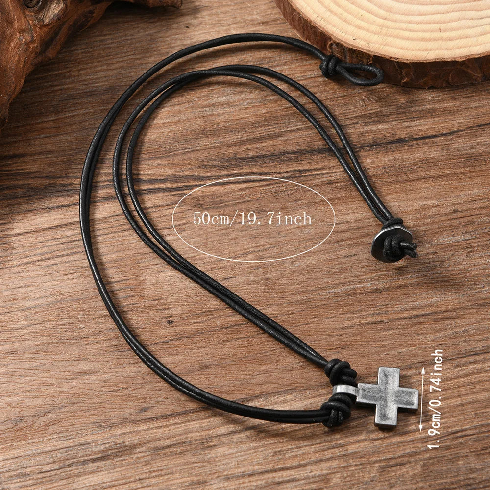 Black cord necklace with a silver cross pendant on a wooden surface