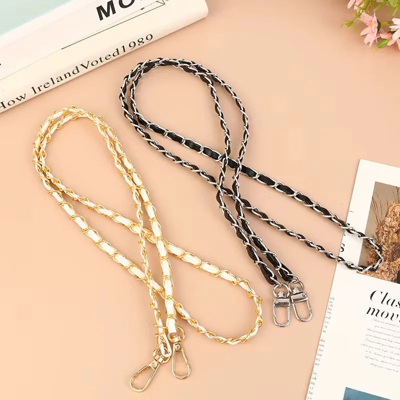 Two chain straps, one gold and one black, on a light surface with a magazine underneath.