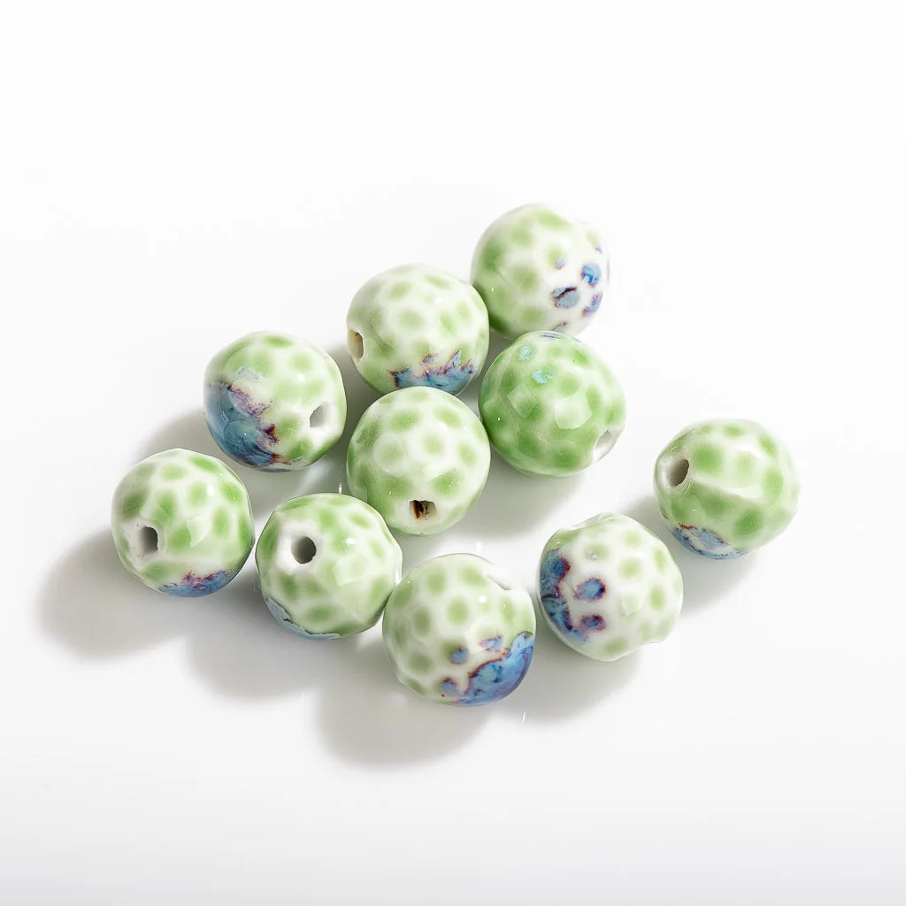 A group of ten round ceramic beads with a light green and white spotted pattern and blue accents, arranged on a plain white background.