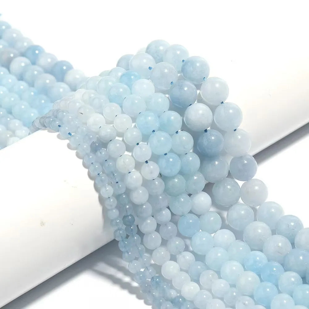 Multiple strands of light blue and white round beads draped over a white cylindrical display on a clean white background.