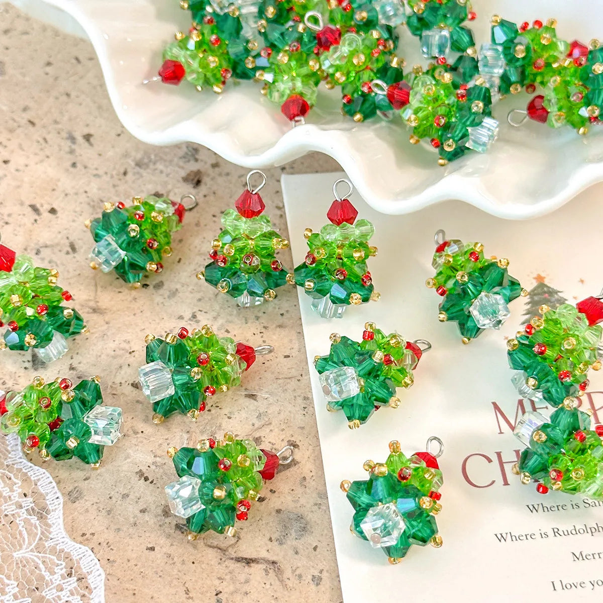 Green beaded Christmas tree charms on a textured surface with a white shell in the background.