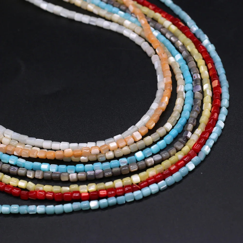Multiple strands of small cylindrical beads in assorted colors, including light blue, red, orange, beige, gray, and white, arranged in a curved stack on a dark background.