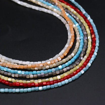 Multiple strands of small cylindrical beads in assorted colors, including light blue, red, orange, beige, gray, and white, arranged in a curved stack on a dark background.