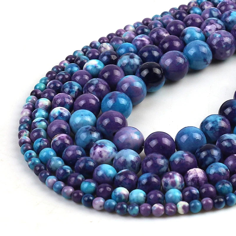 Multiple strands of polished round gemstone beads in shades of blue, purple, and teal, arranged in a curved stack on a white background.