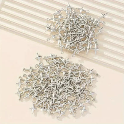 A pile of small silver metal four-pointed star charms with loops at the ends, arranged on a light beige surface with a cream ribbed background.