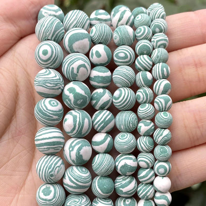 A close-up of multiple strands of round beads held in a person's hand. The beads have a marbled swirl pattern in sage green and white.