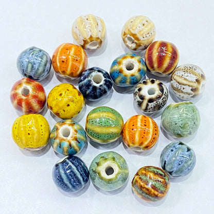 A group of 18 handmade ceramic beads with varied patterns, including stripes, speckles, and swirls in yellow, blue, green, orange, brown, and white, arranged on a plain white background.