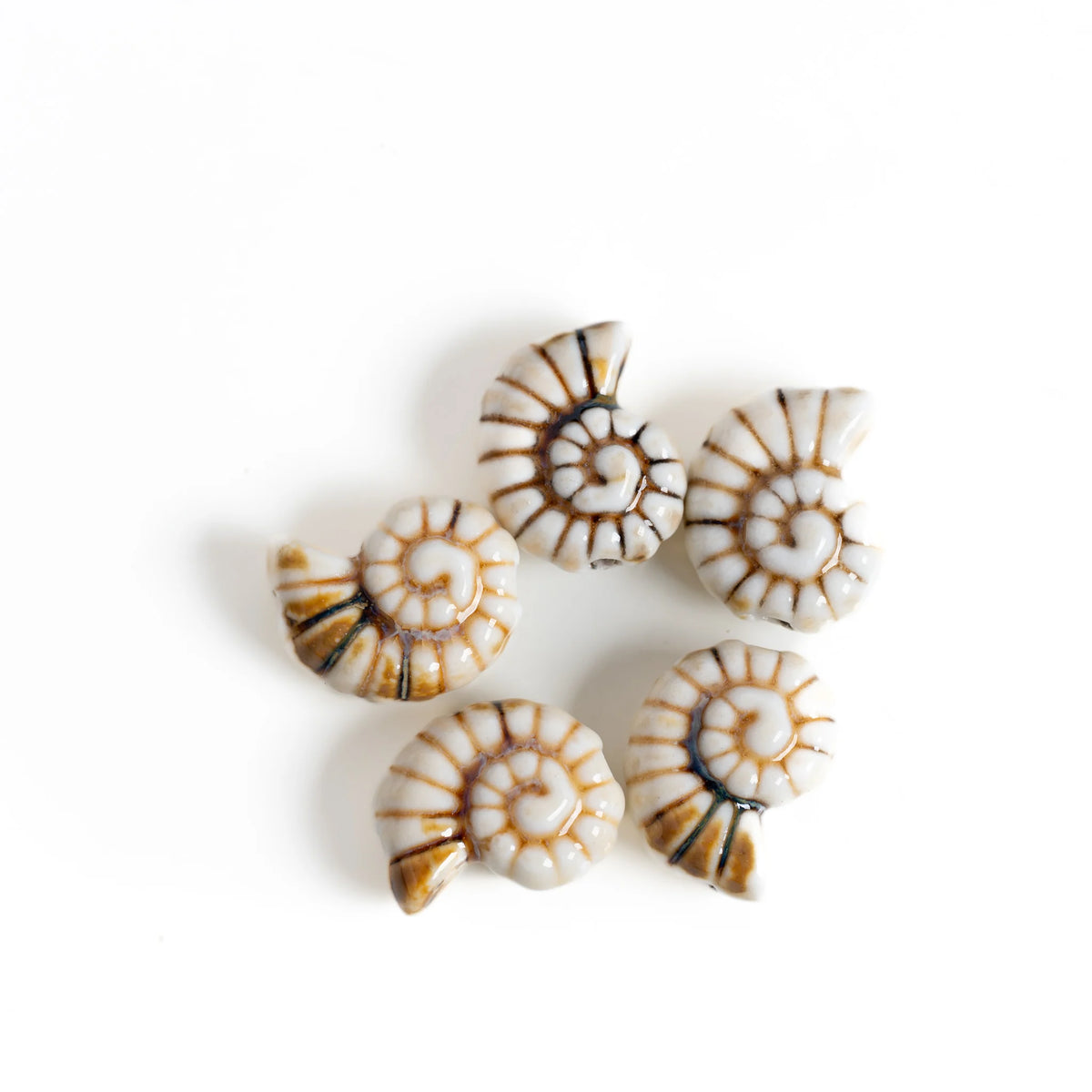 Five small spiral conch shell-shaped beads or charms with a white base and brown spiral stripes, arranged on a plain white background.