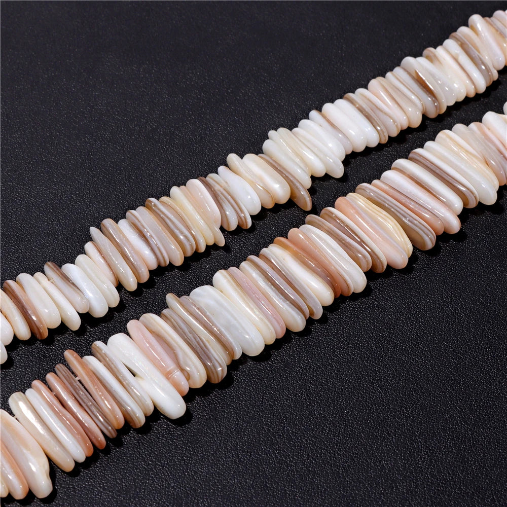 Two strands of natural mother of pearl stone chip beads in shades of cream, beige, and brown, laid diagonally on a dark textured background.