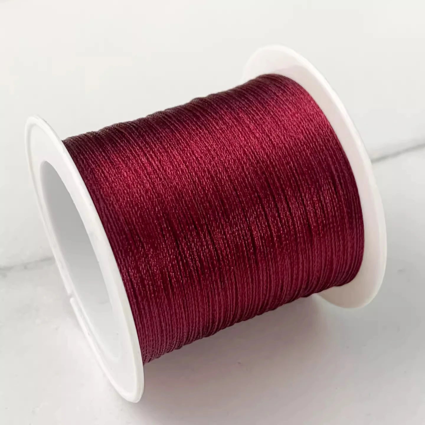 A spool of deep burgundy embroidery thread wound on a white plastic spool, photographed on a light gray surface.