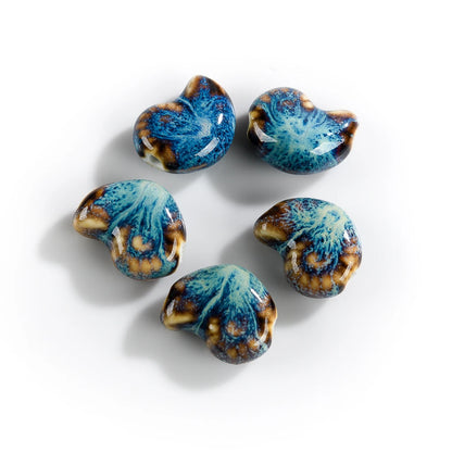 Five small conch-shaped beads with a glossy blue, brown, and cream marbled pattern, arranged on a plain white background.