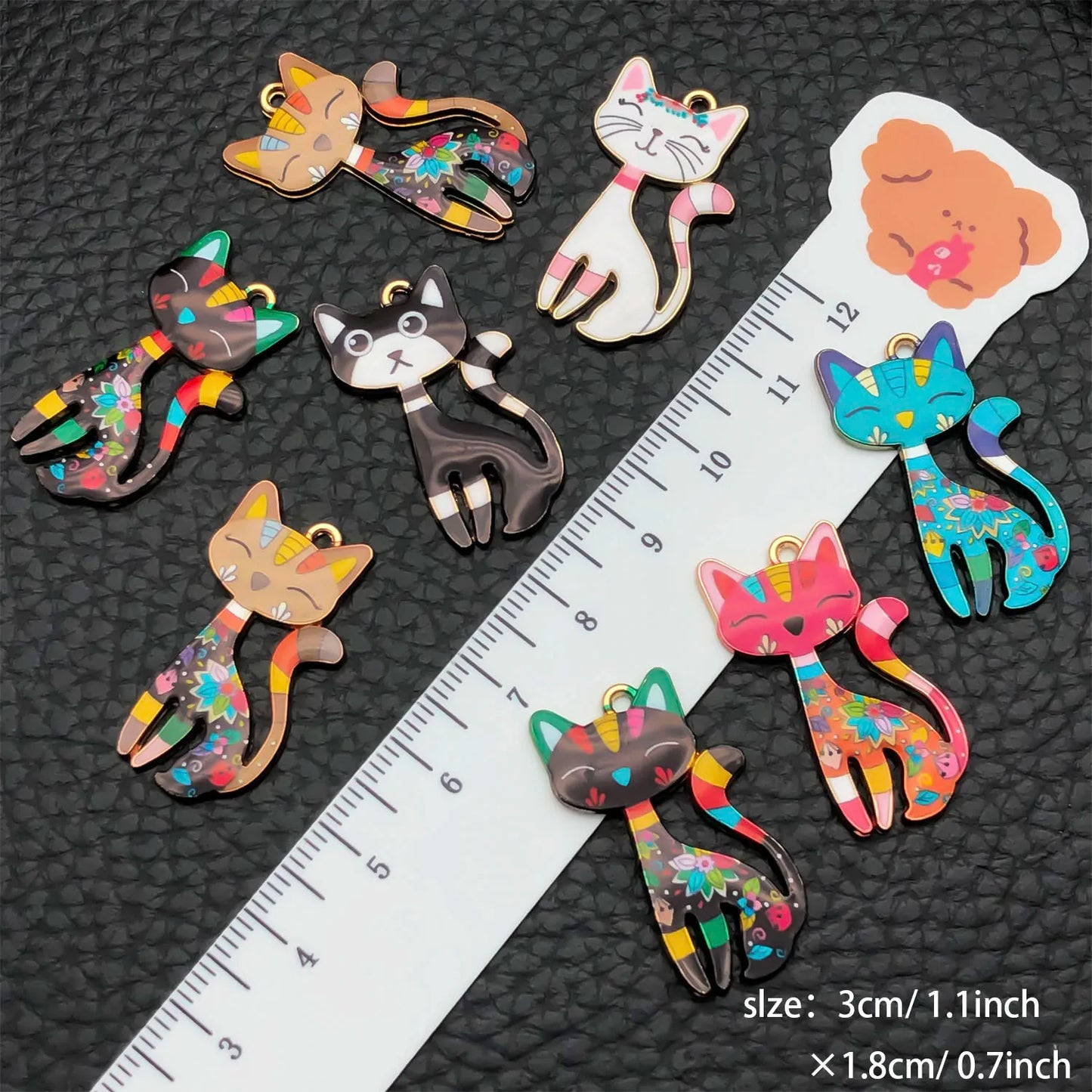 Colorful cat-shaped hair clips on a black textured background with a ruler for scale.