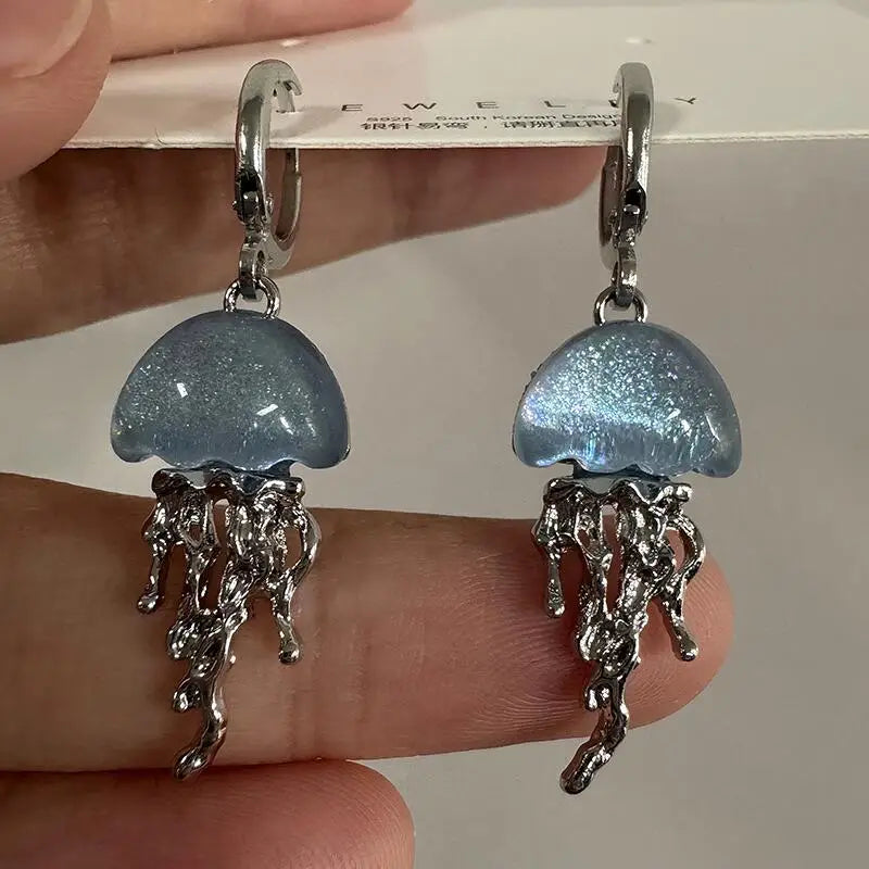 Jellyfish-shaped earrings held by a hand with a blurred background