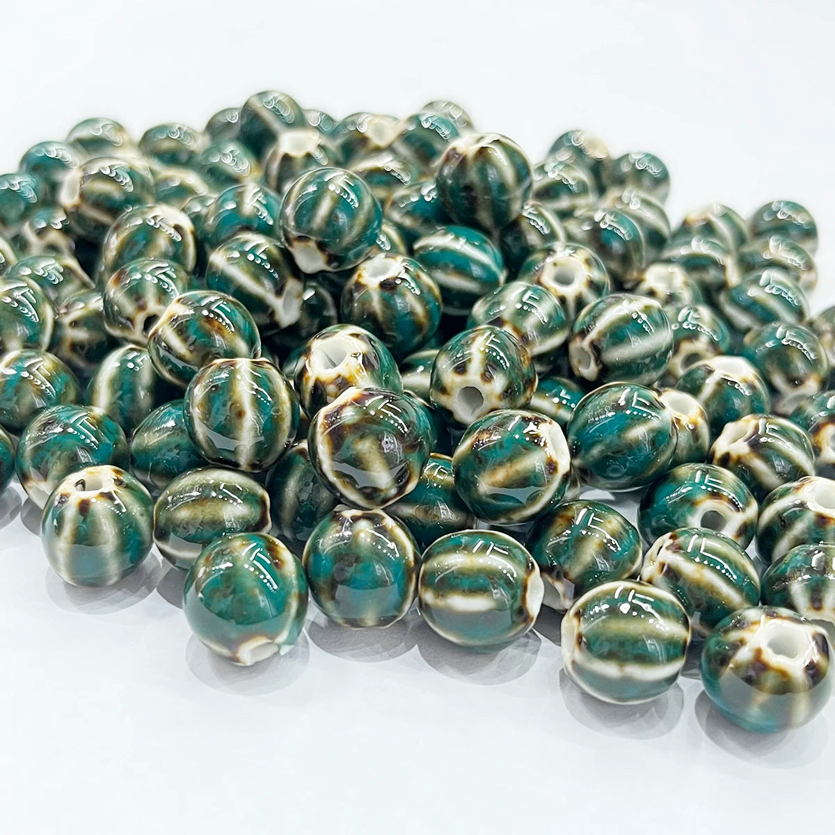 A pile of round, glossy beads with a marbled pattern of dark teal green, cream, and brown on a white background.