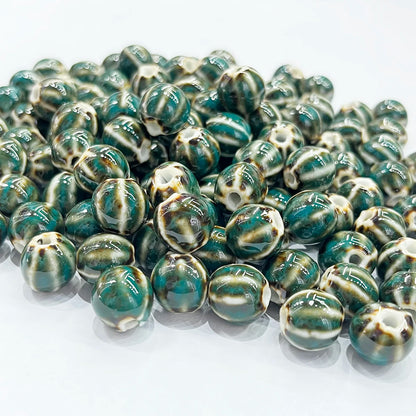 A pile of round, glossy beads with a marbled pattern of dark teal green, cream, and brown on a white background.