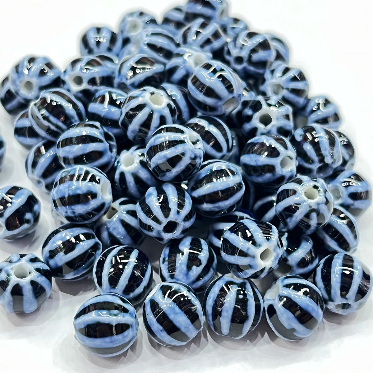 A pile of round glass beads with a glossy black and light blue striped pattern, arranged on a white background.