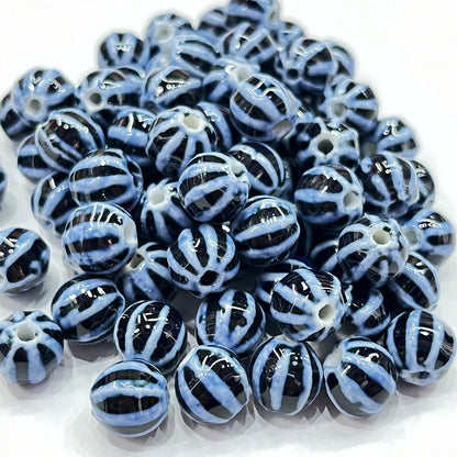 A pile of round glass beads with a glossy black and light blue striped pattern, arranged on a white background.