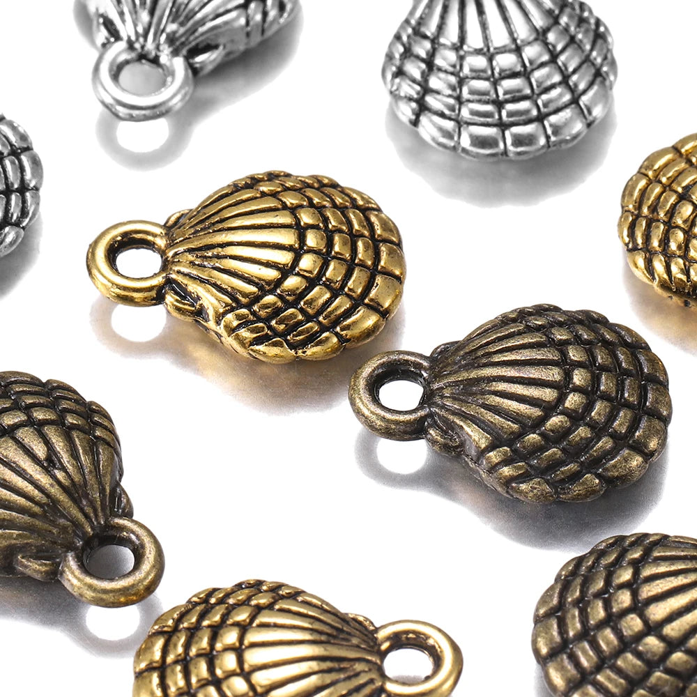 Close-up of multiple shell-shaped jewelry charms in antique gold and silver finishes scattered on a white background.