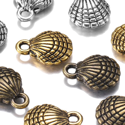 Close-up of multiple shell-shaped jewelry charms in antique gold and silver finishes scattered on a white background.