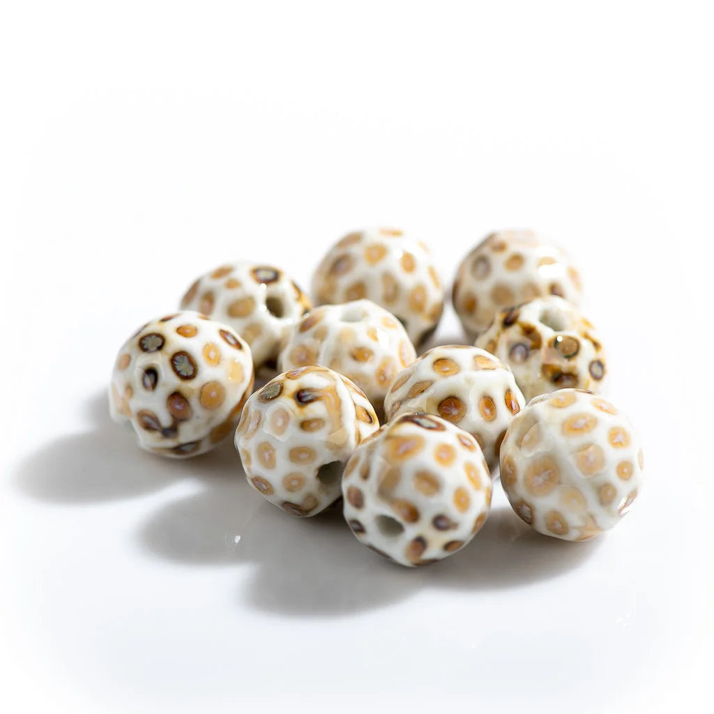A cluster of round, glossy white beads with a textured surface and small tan and dark brown spots, arranged on a clean white background.
