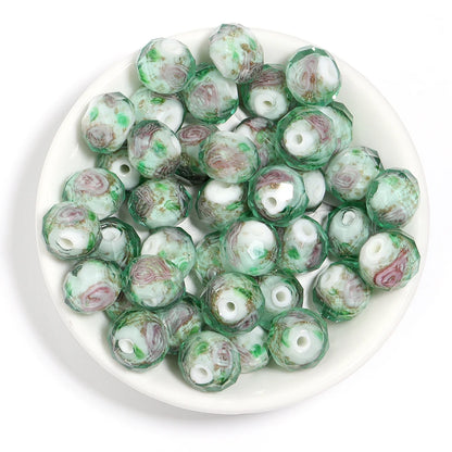 A pile of round glass beads with a swirled pattern of green, white, and dusty pink, displayed on a white plate against a white background.