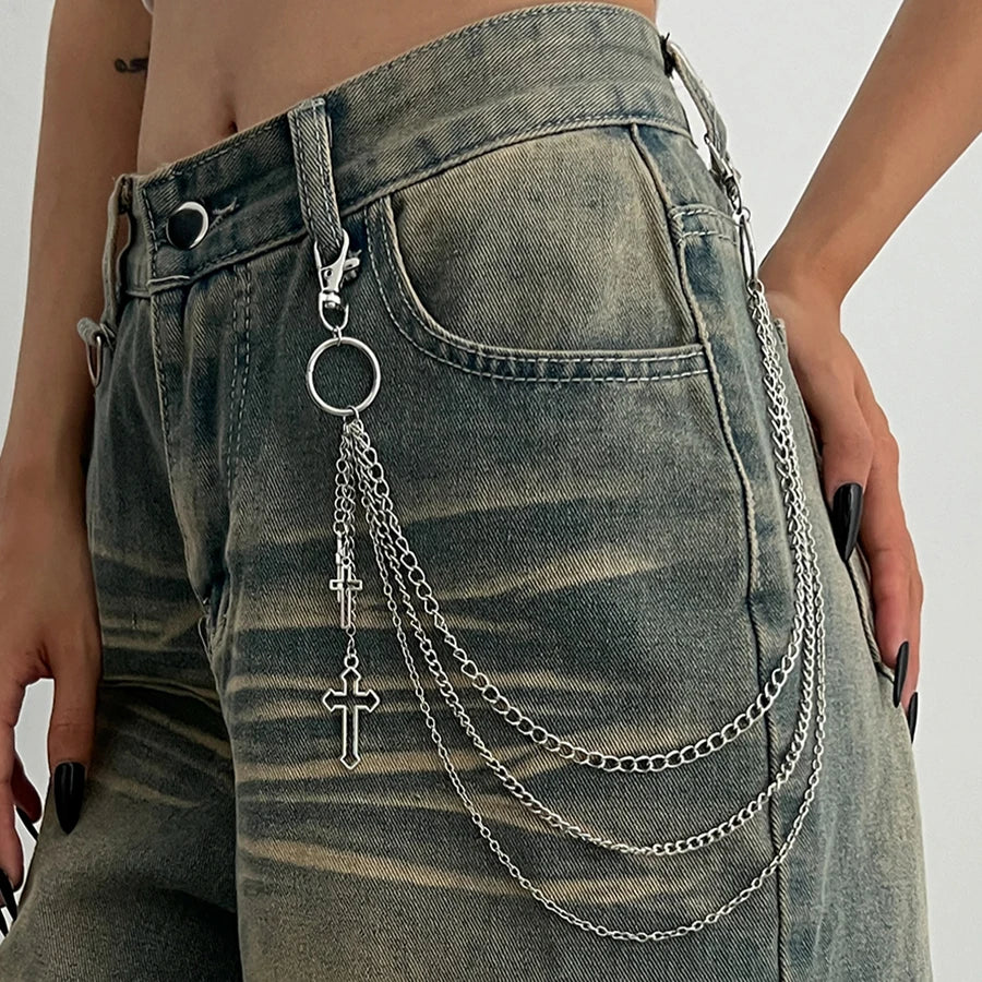 Person wearing a chain with a cross pendant attached to their jeans.