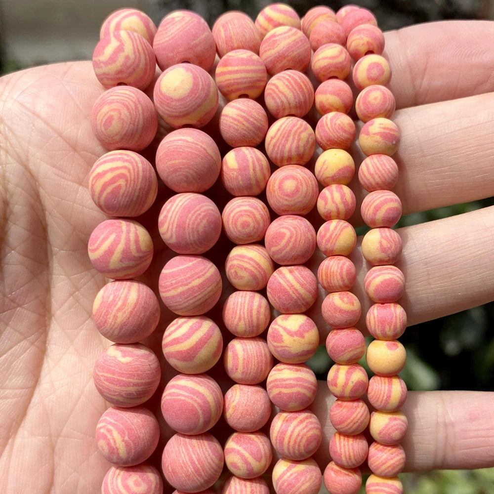 A close-up of a hand holding multiple strands of round wooden beads with pink and yellow swirl patterns.