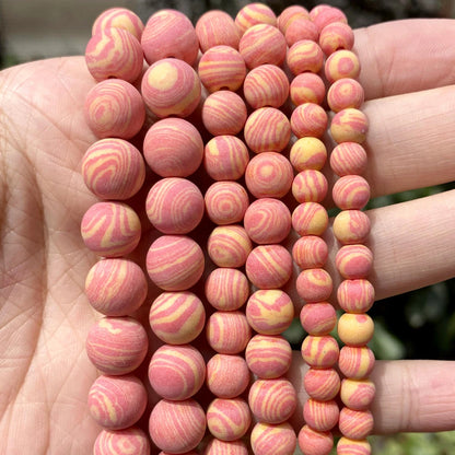 A close-up of a hand holding multiple strands of round wooden beads with pink and yellow swirl patterns.