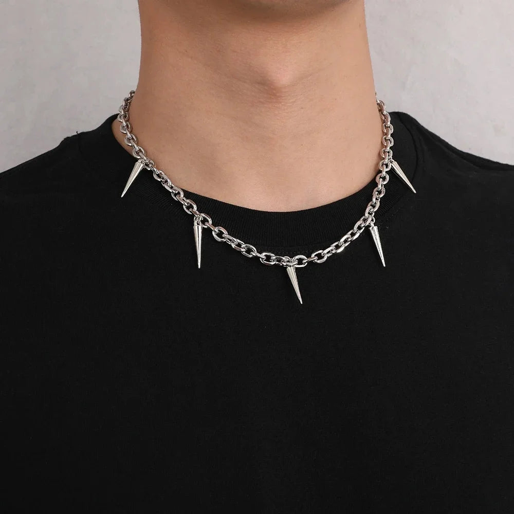 Silver chain necklace with spikes worn by a person on a plain background