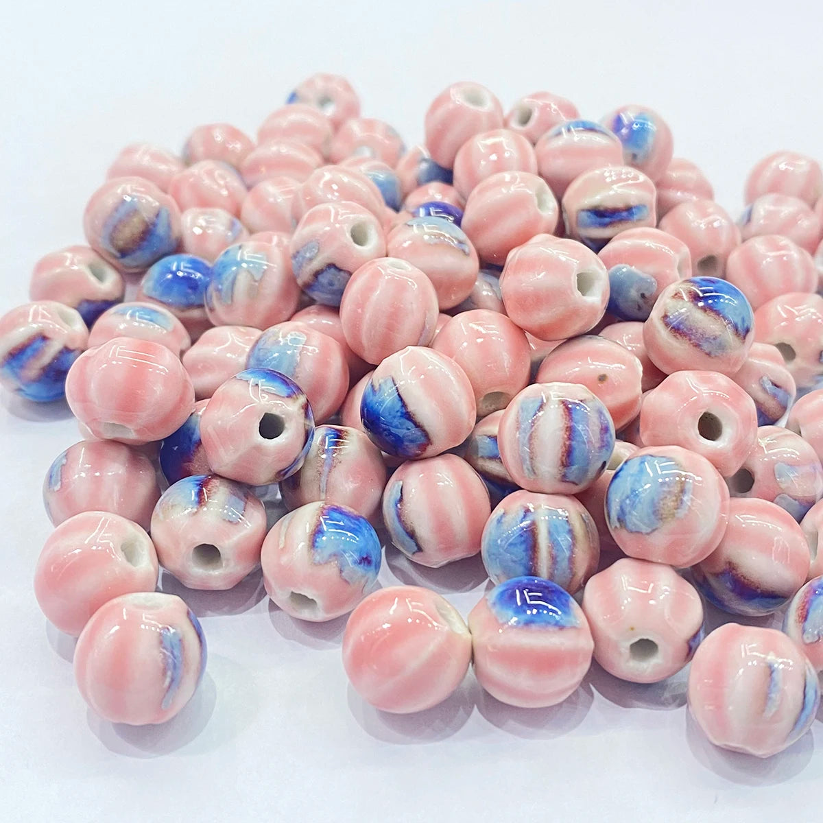 A pile of round glass beads with a pink and white marbled pattern and blue accents, displayed on a clean white background.