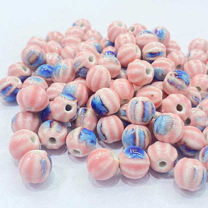 A pile of round glass beads with a pink and white marbled pattern and blue accents, displayed on a clean white background.