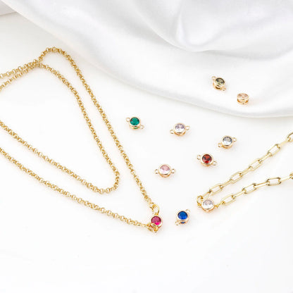 Gold chain necklaces and matching stud earrings with small round multicolor gemstone settings, arranged on a white fabric background.