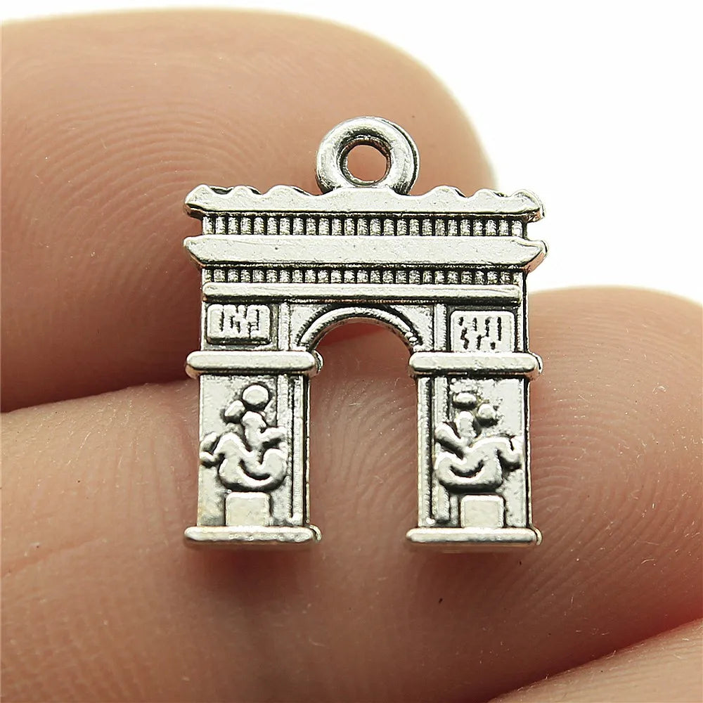 Silver arch-shaped pendant held between two fingers. Travel charms for jewelry making featuring airplane, passport, suitcase and camera charms.