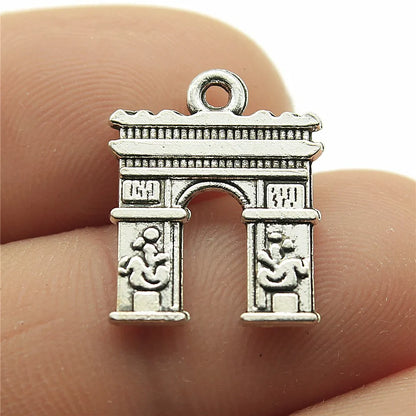 Silver arch-shaped pendant held between two fingers. Travel charms for jewelry making featuring airplane, passport, suitcase and camera charms.