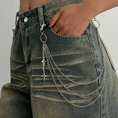 A close-up of a person wearing distressed gray denim jeans with a silver metal chain accessory hanging from the waistband and draped across the back pocket area. The chain includes rings, multiple strands of links, and small star-shaped charms.