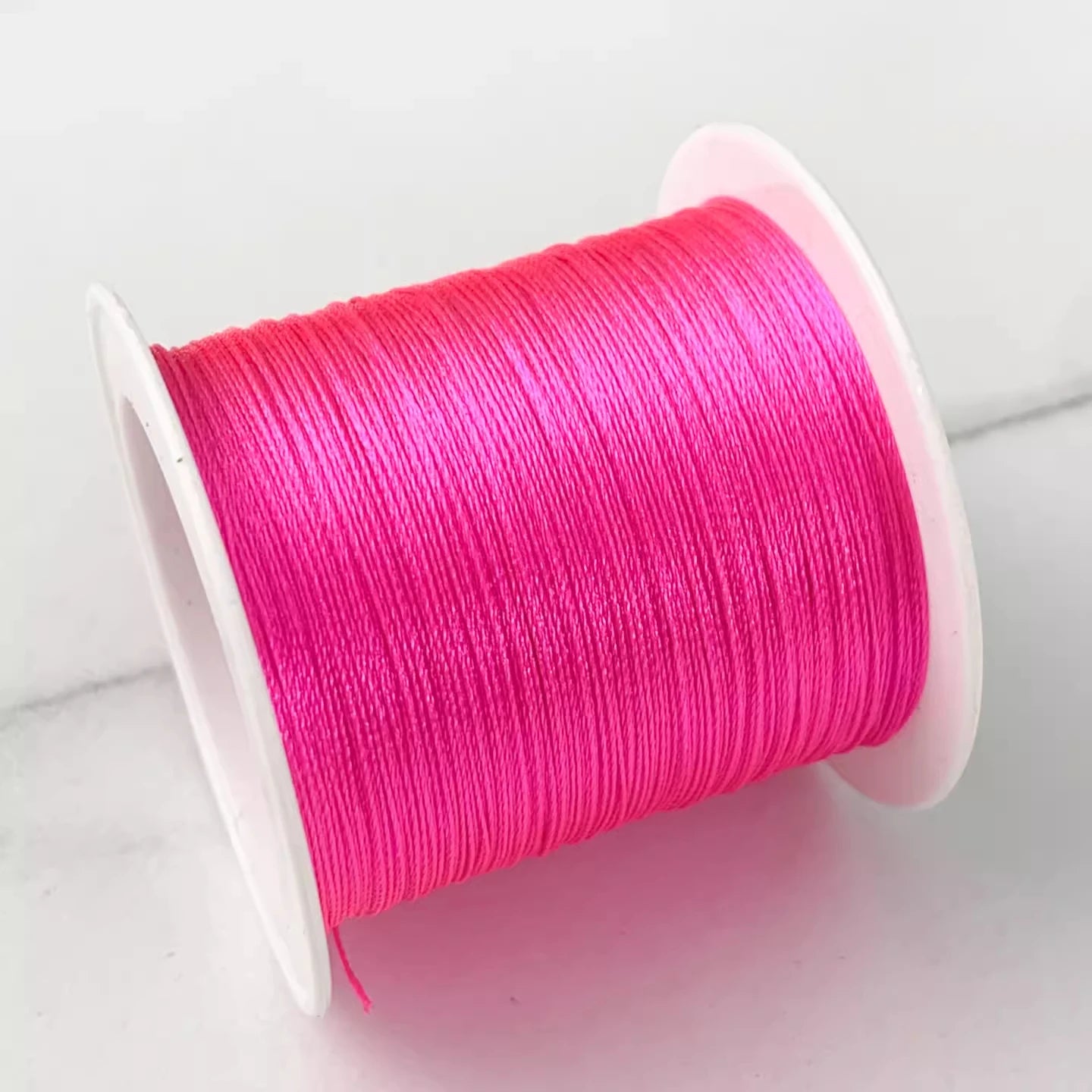 A spool of bright hot pink embroidery thread wound tightly on a white plastic spool, set against a clean white background.
