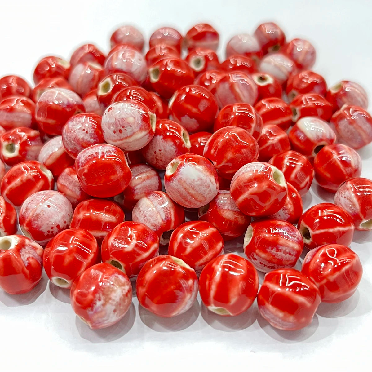 A pile of glossy red and white marbled glass beads with small green accents, photographed on a clean white background.
