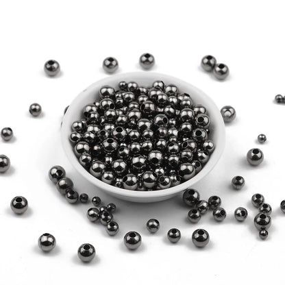 Small metallic dark gray beads with hollow centers, shown piled in a white shallow dish with a few scattered around on a white background.