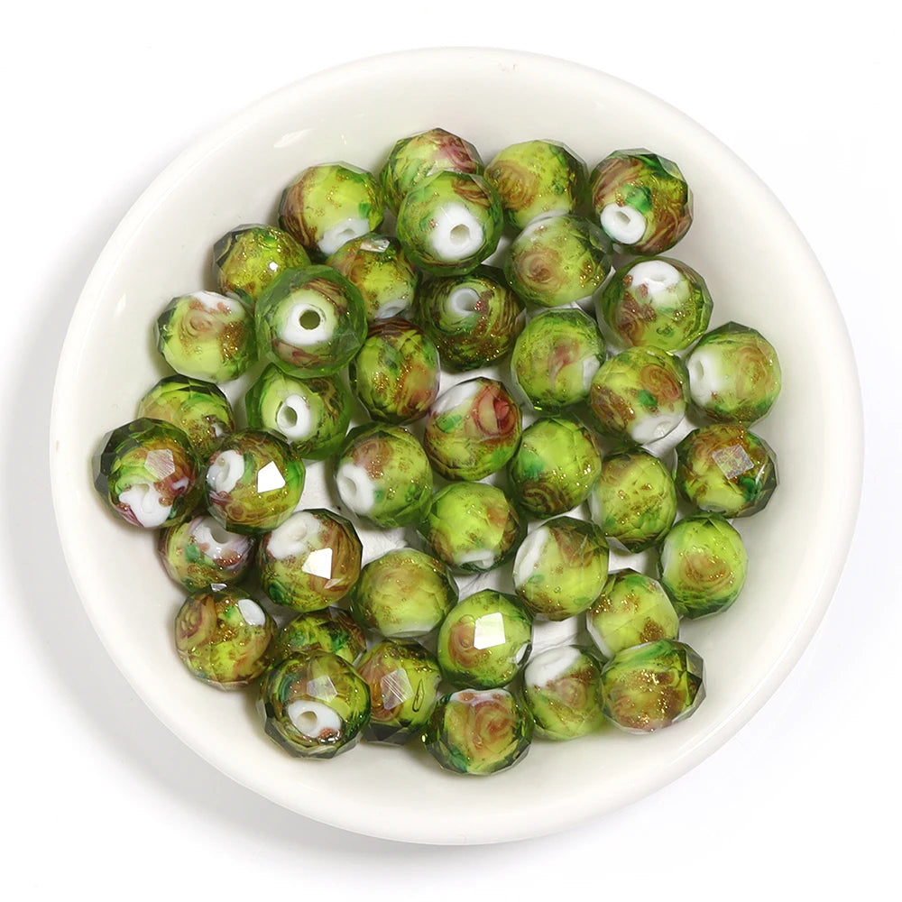 Green marbled faceted glass beads with white centers, displayed in a small white ceramic bowl on a white background.