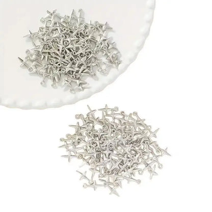 Small silver metal findings or decorative charms scattered on a white background, with a pile also placed on the edge of a white plate.
