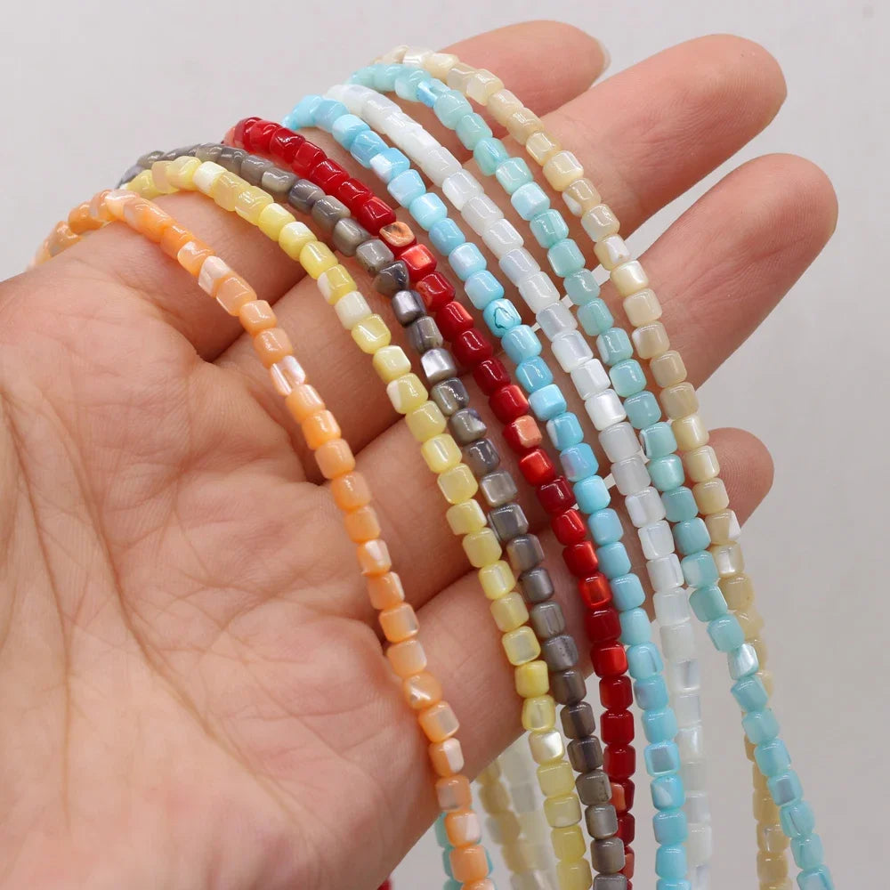 A hand holding several strands of small faceted shell beads in assorted colors, including orange, yellow, gray, red, white, and light blue, against a plain light background.
