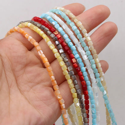 A hand holding several strands of small faceted shell beads in assorted colors, including orange, yellow, gray, red, white, and light blue, against a plain light background.