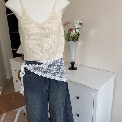 Mannequin wearing a beige knit tank top, blue jeans with lace trim, and a white vase with flowers in the background.