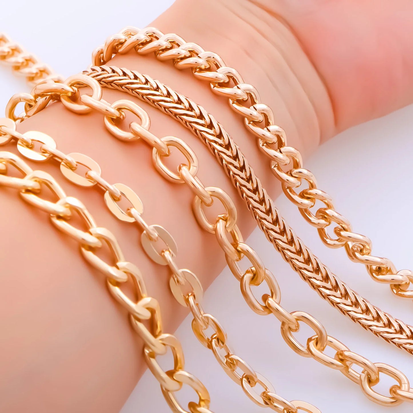 Close-up of a hand wearing multiple gold-tone chain bracelets, including curb, rope, and link styles, against a clean white background.