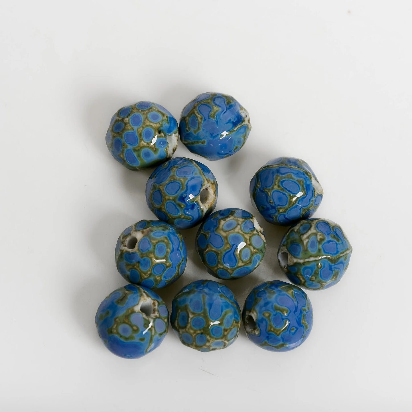 Nine handmade ceramic beads with a blue and green mosaic pattern, arranged on a plain white background.
