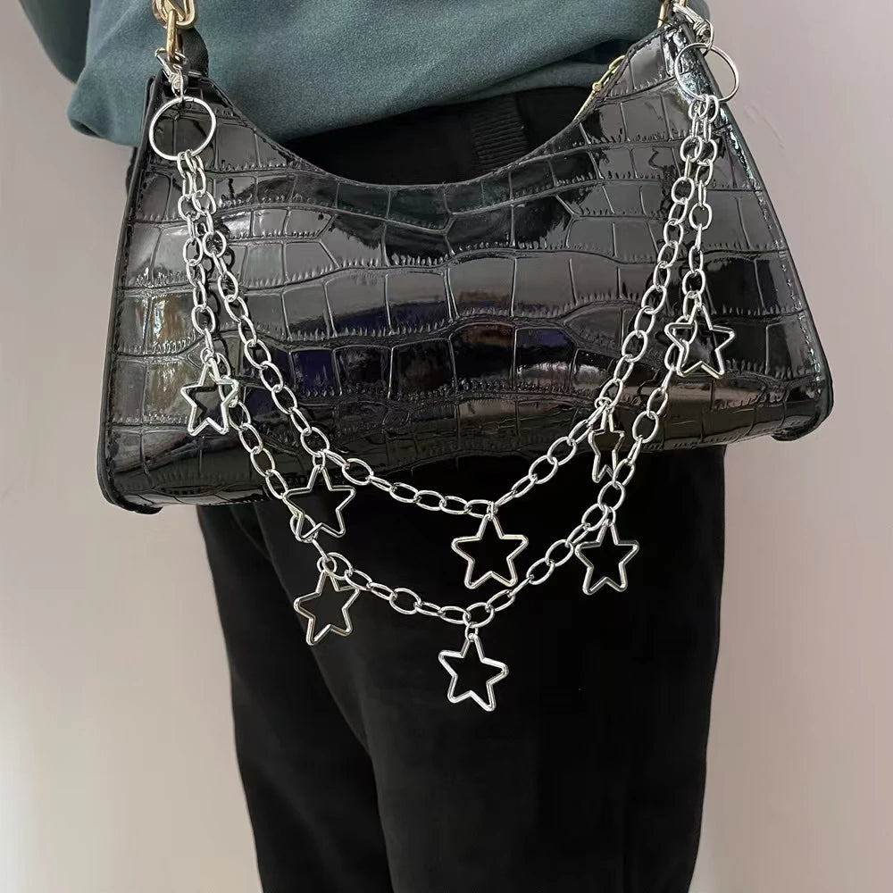Black crocodile-patterned handbag with star-shaped chain detail held by a person.