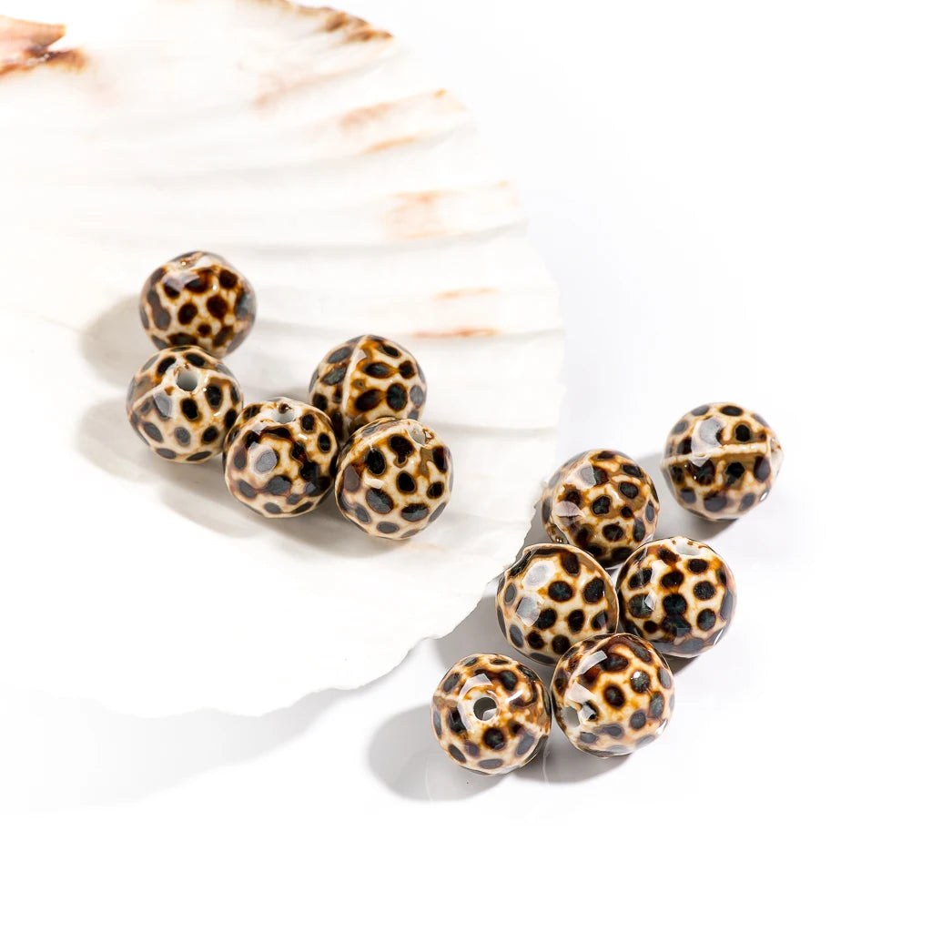 Ten round glass beads with a leopard print pattern in black, brown, and beige, arranged on a white background with a decorative white shell.